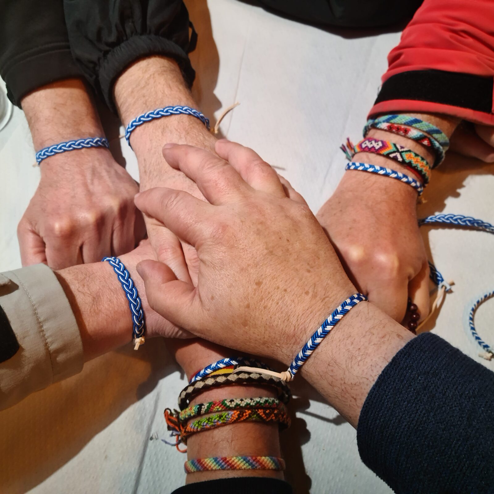 Hände einer Segelcrew mit geflochtenen Armbändern als Teamritual